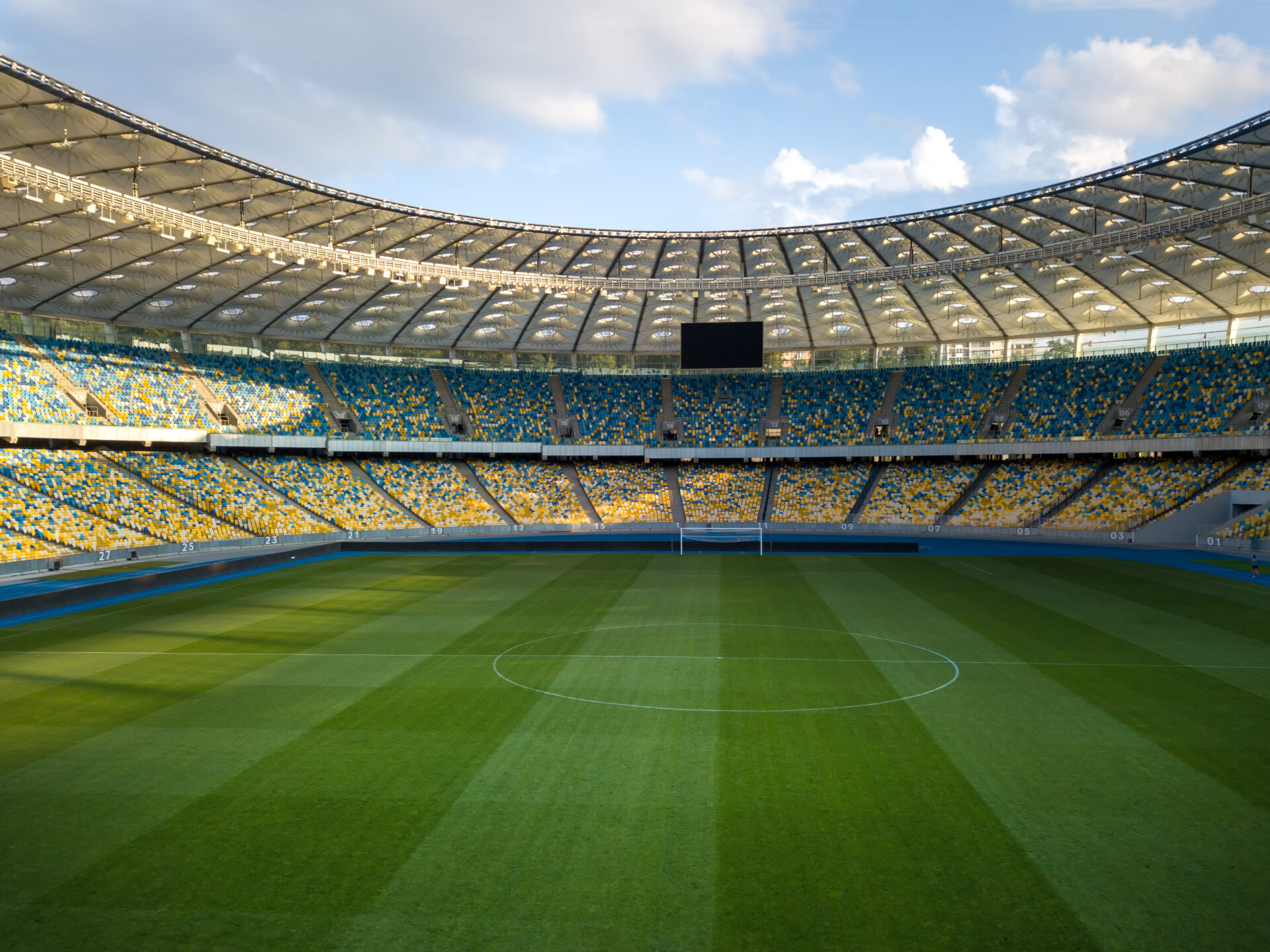 Green field with blue-yellow stands against the blue sky with clouds